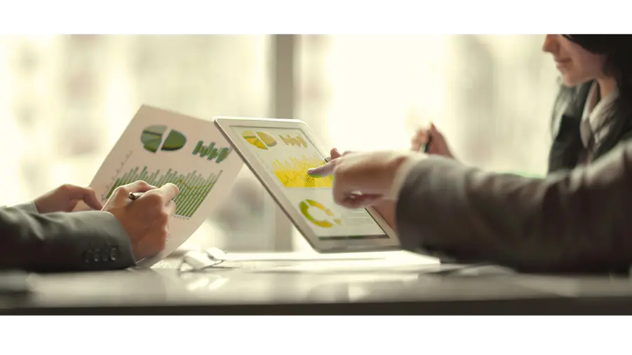 Profissionais de procurement analisando comparativos de mercado em reunião estratégica com gráficos em tablet e papel.