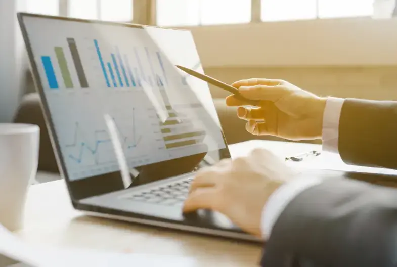 Análise de dados e gráficos financeiros em laptop durante reunião de procurement focada em reajuste contratual estratégico.